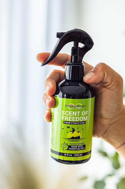 Hand holding Scent of Freedom plant-based room spray by Aroma Sanctuary with natural greenery background