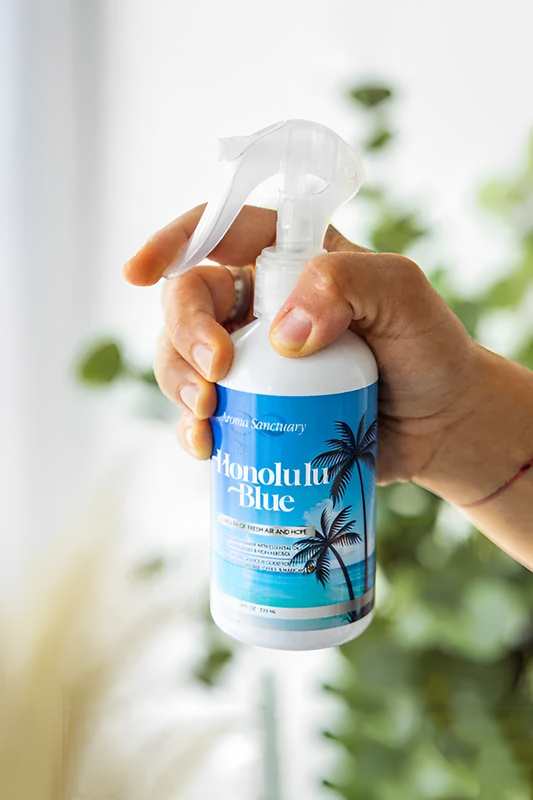 Hand holding Honolulu Blue plant-based room spray by Aroma Sanctuary with a natural greenery background
