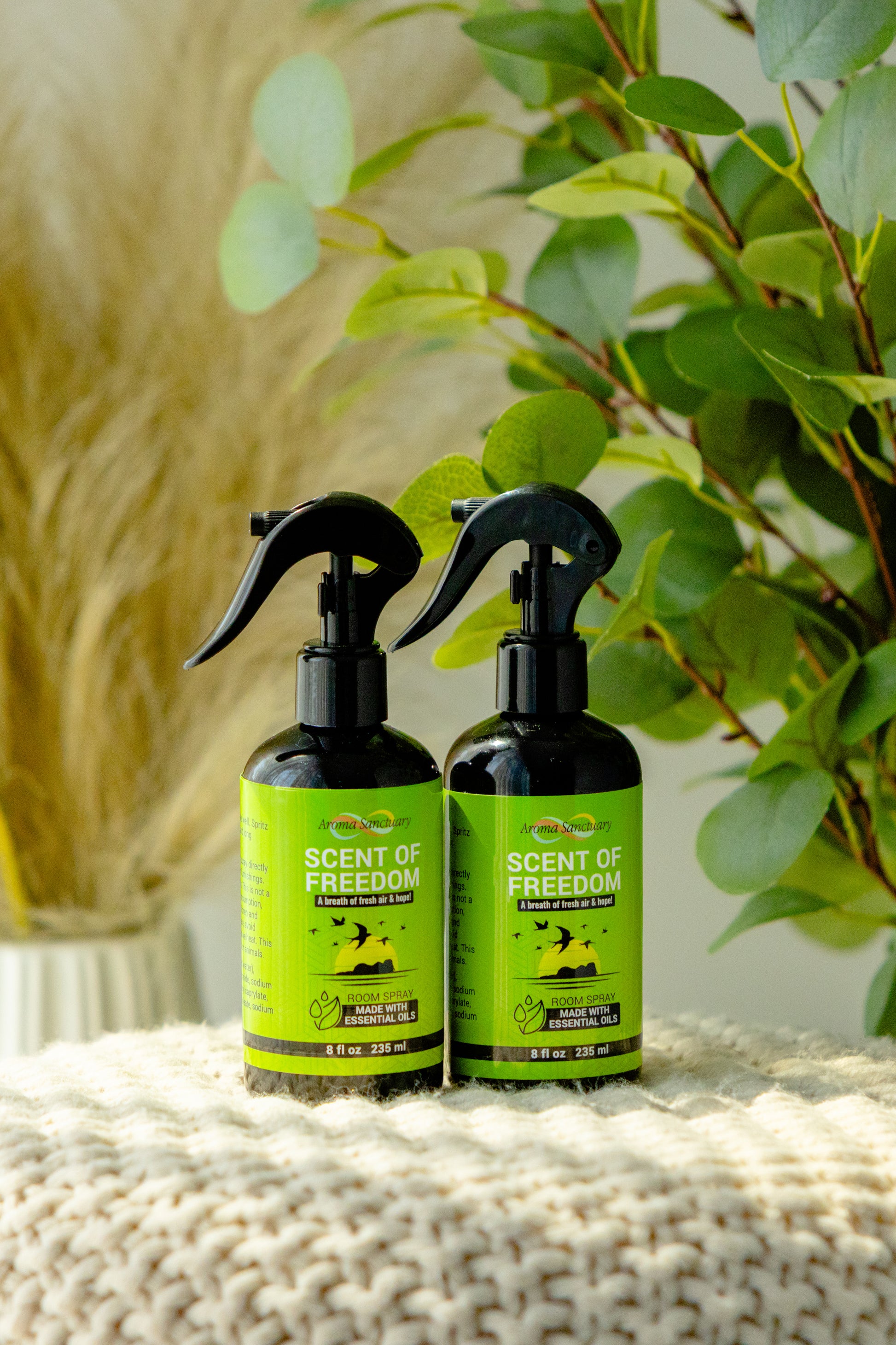 Two Scent of Freedom plant-based room sprays by Aroma Sanctuary, placed on a textured surface with greenery in the background