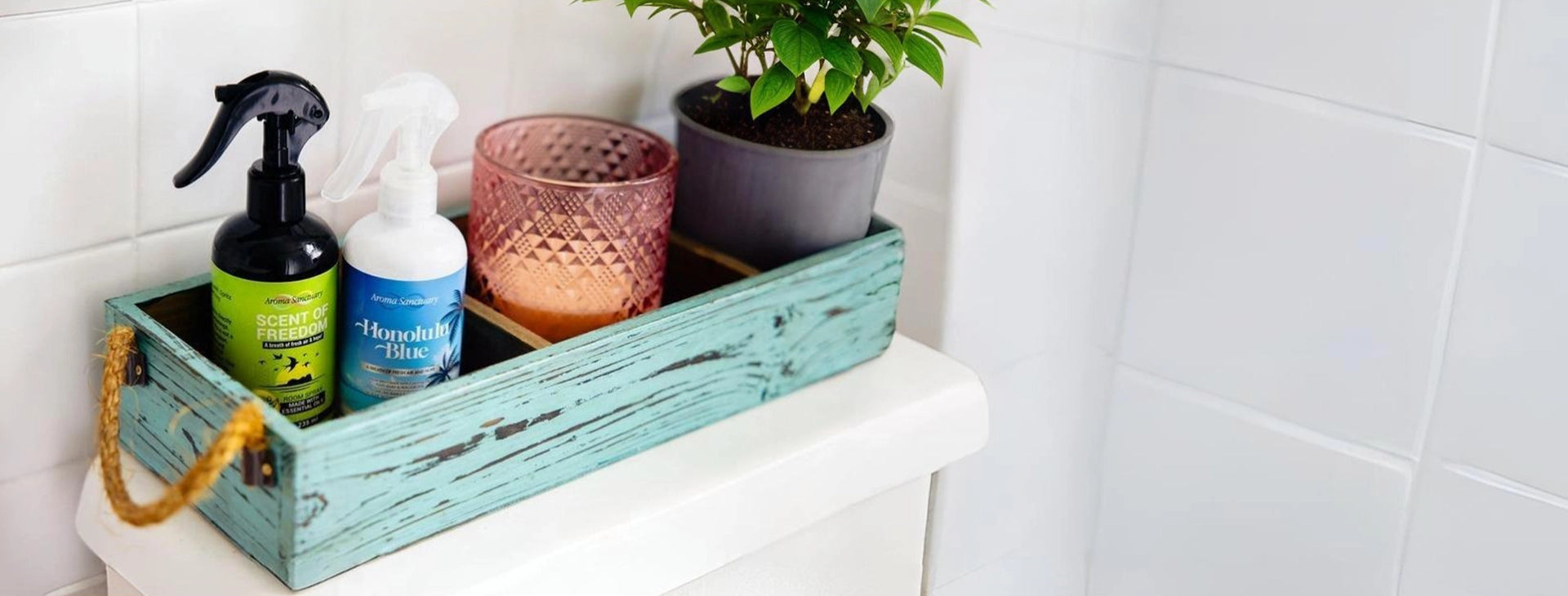 Scent of Freedom and Honolulu Blue plant-based room sprays by Aroma Sanctuary, placed in a wooden tray alongside potted plants in a bathroom setting