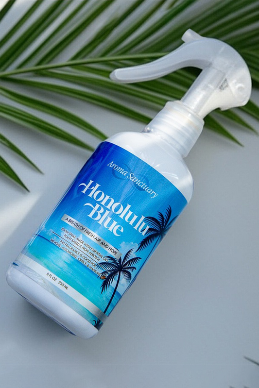 Honolulu Blue plant-based room spray by Aroma Sanctuary on a white surface with palm leaves