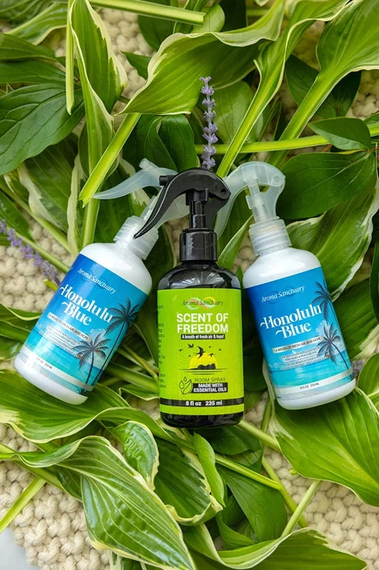 Scent of Freedom and Honolulu Blue plant-based room sprays by Aroma Sanctuary, arranged on green leaves 