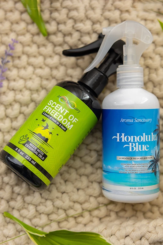 Scent of Freedom and Honolulu Blue plant-based room sprays by Aroma Sanctuary, placed on a textured surface with natural greenery